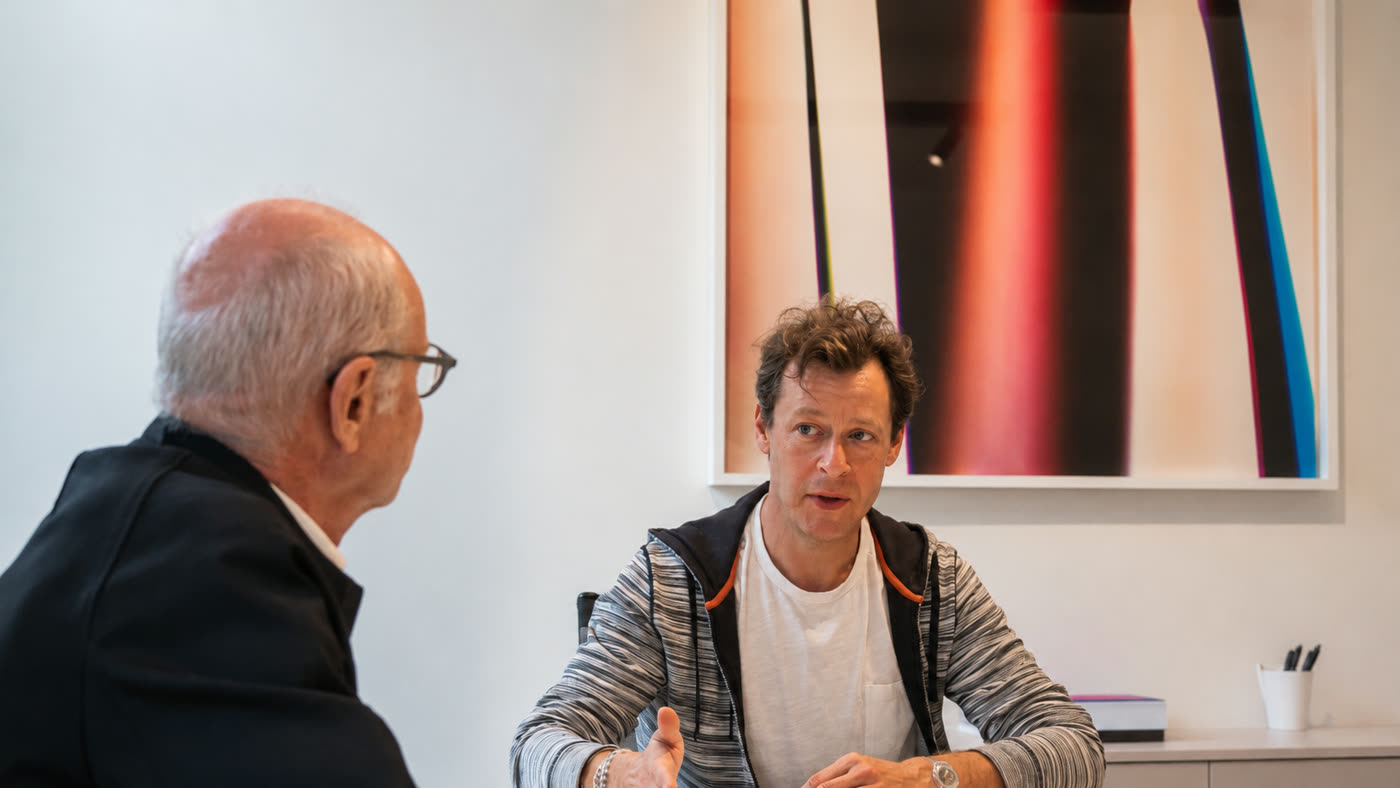 Alexandre Daletchine coaching a senior executive one to one, talking across a table beneath a large abstract painting.